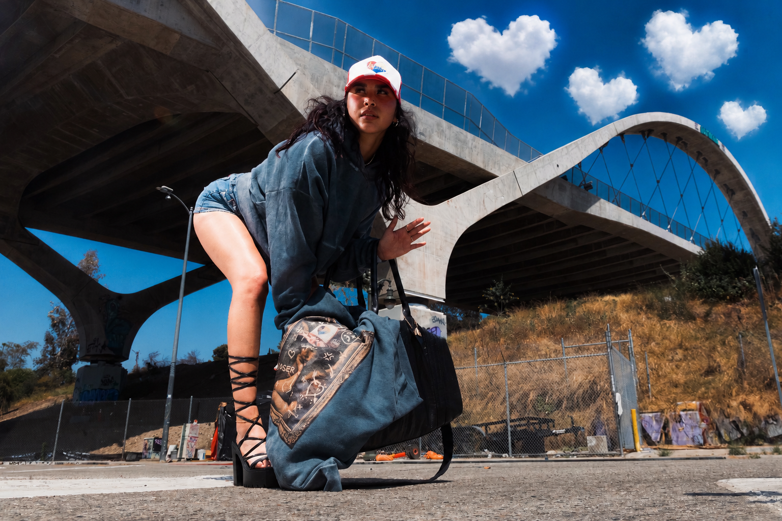 Person posing with a large bag under a modern architectural structure with a blue sky.